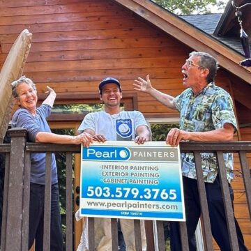 Two clients with painter, all three smiling and laughing, holding a Pearl Painters sign while standing on their deck after the exterior was professionally stained