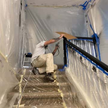 A man is painting the stairs in a house with plastic covering, as an interior painter in Portland.