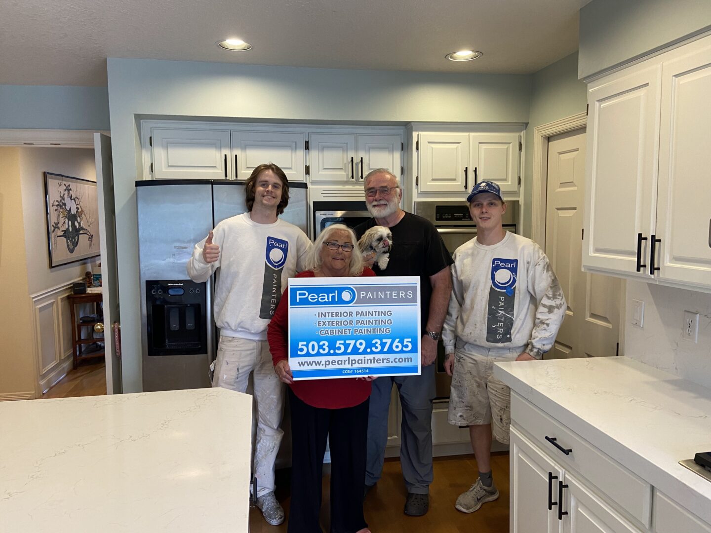 A group of people standing in front of a white kitchen, showcasing their expertise in cabinet painting to transform the space.