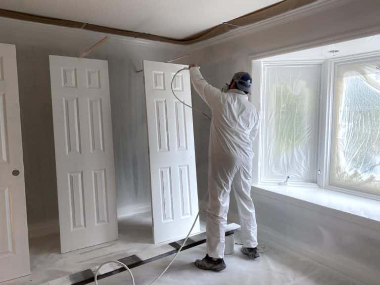 Interior painter in Portland uses paint sprayer with white paint on doors inside a room