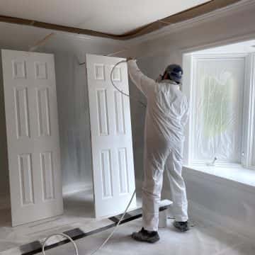 A man painting white doors in a room with glossy oil.