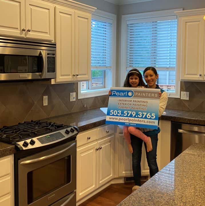 Two women holding a sign in a kitchen, featuring SW Portland.