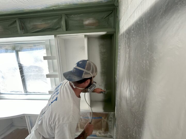 A painter spraying paint on a wall in a kitchen.