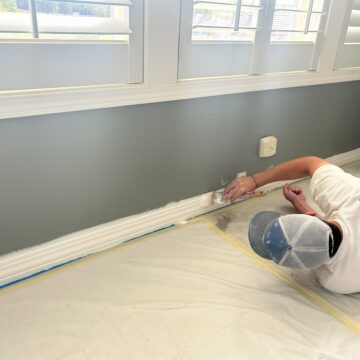A professional painting a room with white paint, focusing on interior trim and doors.