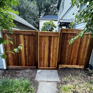 A wooden gate with side panels stands between two houses in Chadderton; Pearl Painters could paint or stain this for you.