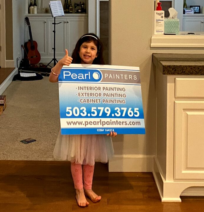 Girl in tutu indoors gives thumbs up, holding Pearl Painters sign with contact info; Portland painter and painting services.