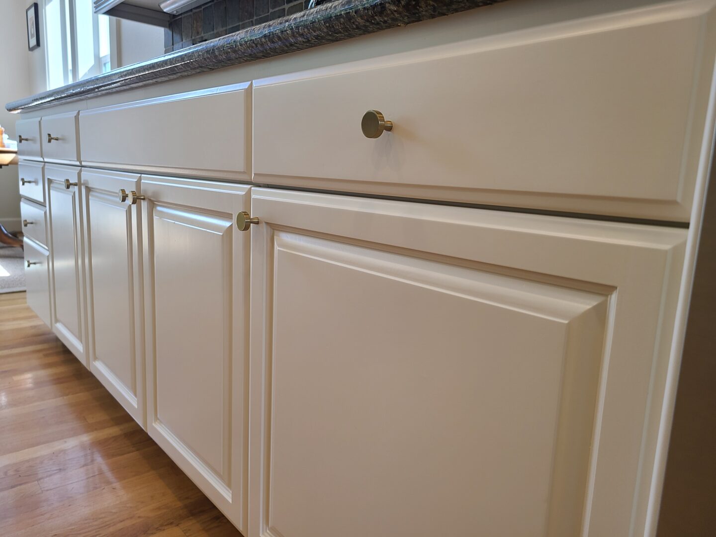 White painted cabinets with silver handles and dark countertop on wood floor, by Pearl Painters, Portland.