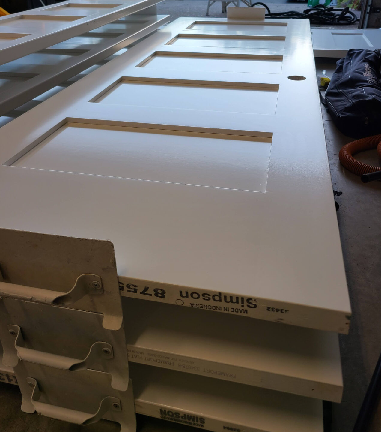 White doors with rectangular panels stacked on supports, ready for painting by Pearl Painters in a Portland workshop.