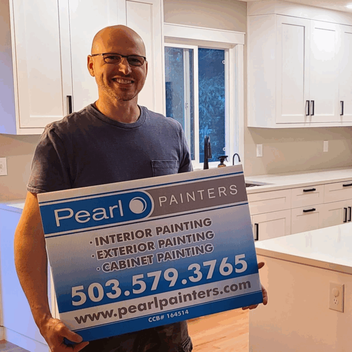 Man in kitchen holds Pearl Painters sign for painting services; mentions interior, exterior, cabinets, and Portland contact info.
