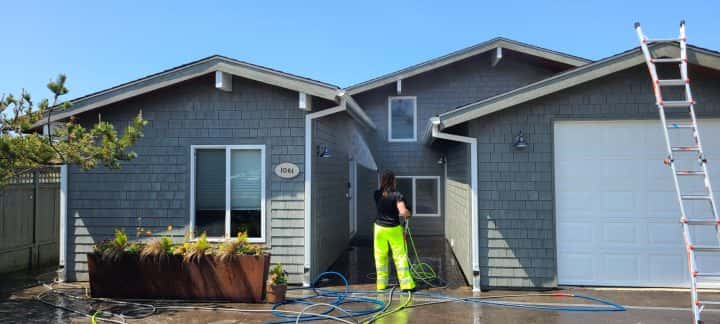 A man cleaning the exterior of the Manzanita Beach House using a ladder.