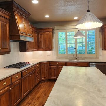 Kitchen with wooden cabinets, marble counters, stainless appliances, island, pendant lights; painted by Pearl Painters in Portland.