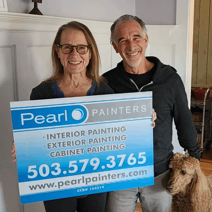 Two adults hold a Pearl Painters sign with contact info next to a brown poodle in a Portland home.