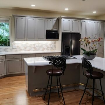 Modern kitchen interior with gray cabinets, white countertops, a built-in refrigerator, and an island with bar stools.