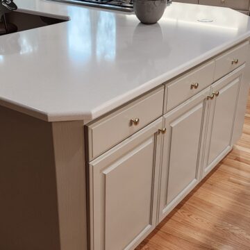 Modern kitchen island with white countertop and beige cabinetry, featuring gold handles, set on a hardwood floor.