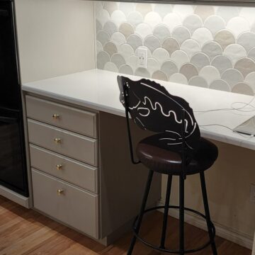 A small kitchen desk area with white cabinets, a built-in oven, and a high stool.