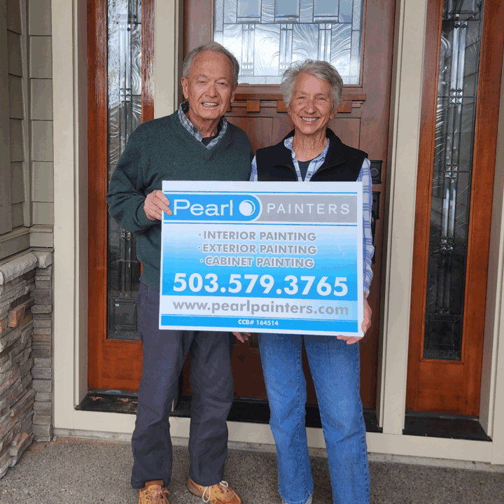 Two people in Portland hold a Pearl Painters sign with painting services and contact info.