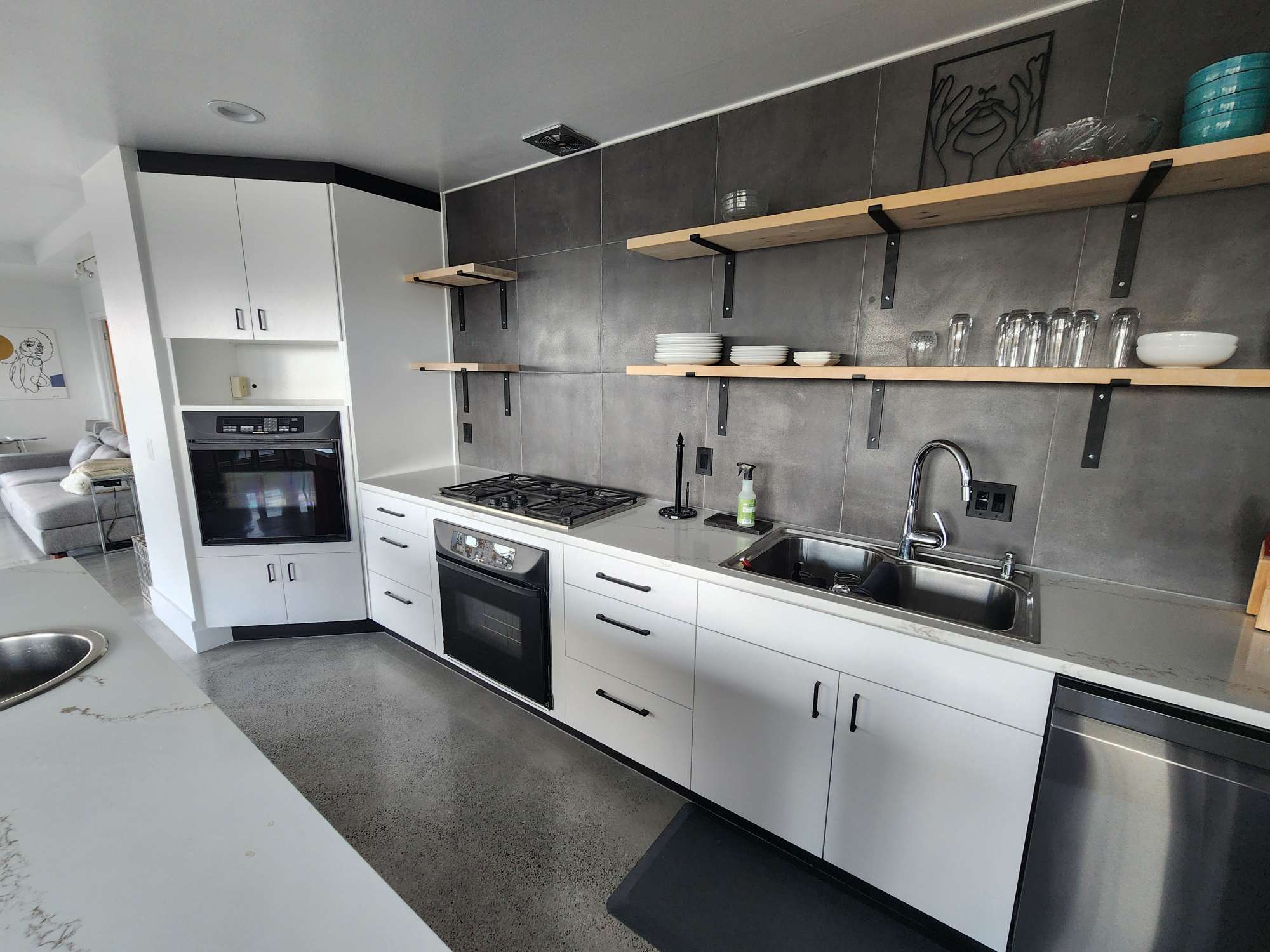 Modern Isadore kitchen in Portland: white cabinets, open wooden shelves, gas stove, built-in oven, sink, dishwasher, and gray tile backsplash. Ideal for April 2025 renovations. Pearl Painters offers painting services for this type of space.