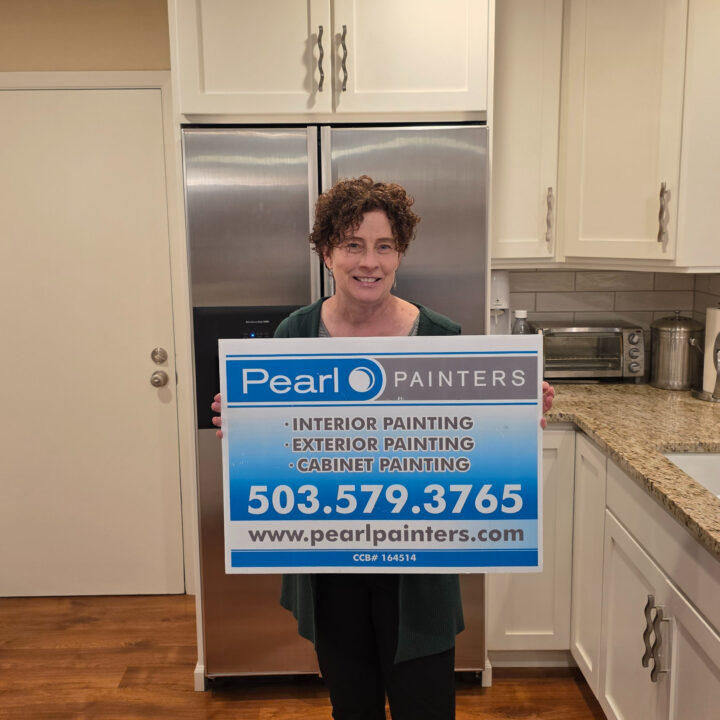Person in kitchen holds Pearl Painters sign for painting services. Painter info, phone, and website shown. Likely in Portland.
