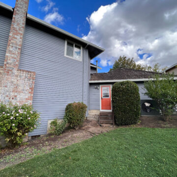 A Beaverton home in the Cooper Mountain Neighborhood with a blue door and bushes in the yard.