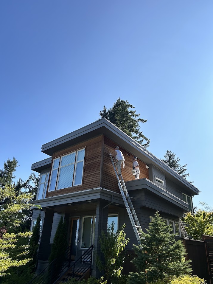 In July 2025, two painters from Pearl Painters paint a modern Shimek house exterior on ladders in Portland under blue sky.