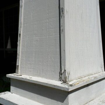 Close-up of a worn, white-painted wooden column base with peeling paint on a stone foundation, indicating this exterior in Portland needs new painting and caulking by a painter such as Pearl Painters.