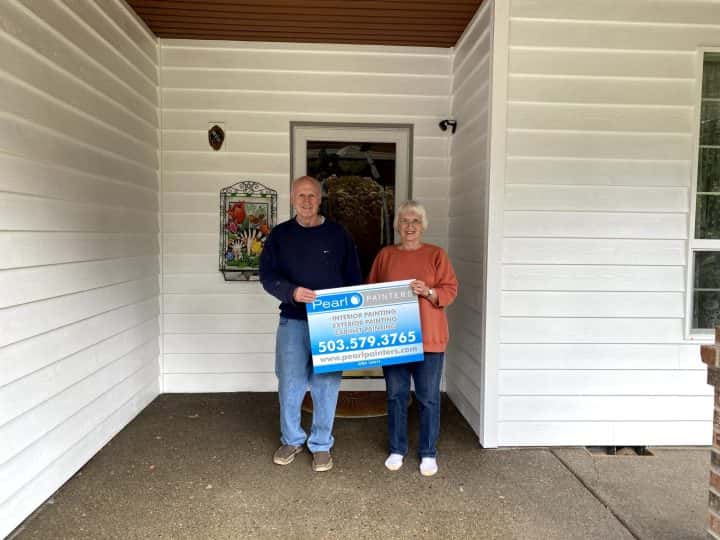 Two people standing in front of a house in Beaverton, holding a sign.