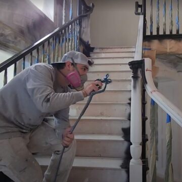 A painter using a paint sprayer to paint a staircase.