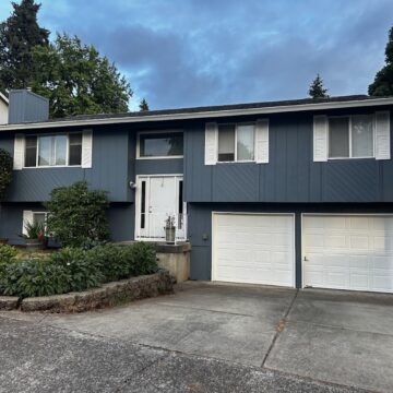A two-story blue house with white trim and double garage doors was painted by Pearl Painters in Portland.