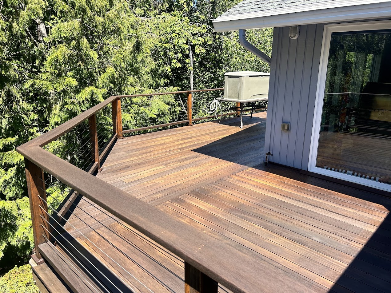 A Shainsky wooden deck with metal cable railing is attached to a house in Portland, overlooking green trees in June 2025 sunlight. Pearl Painters is the local painting contractor.