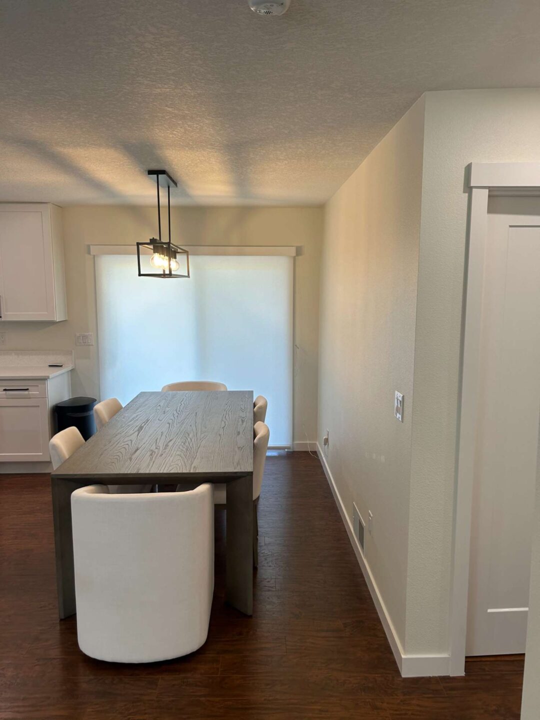 A painter from Pearl Painters in Portland painted this modern dining room, featuring a wooden table, six white chairs, a rectangular light fixture, and sliding glass doors with closed blinds.