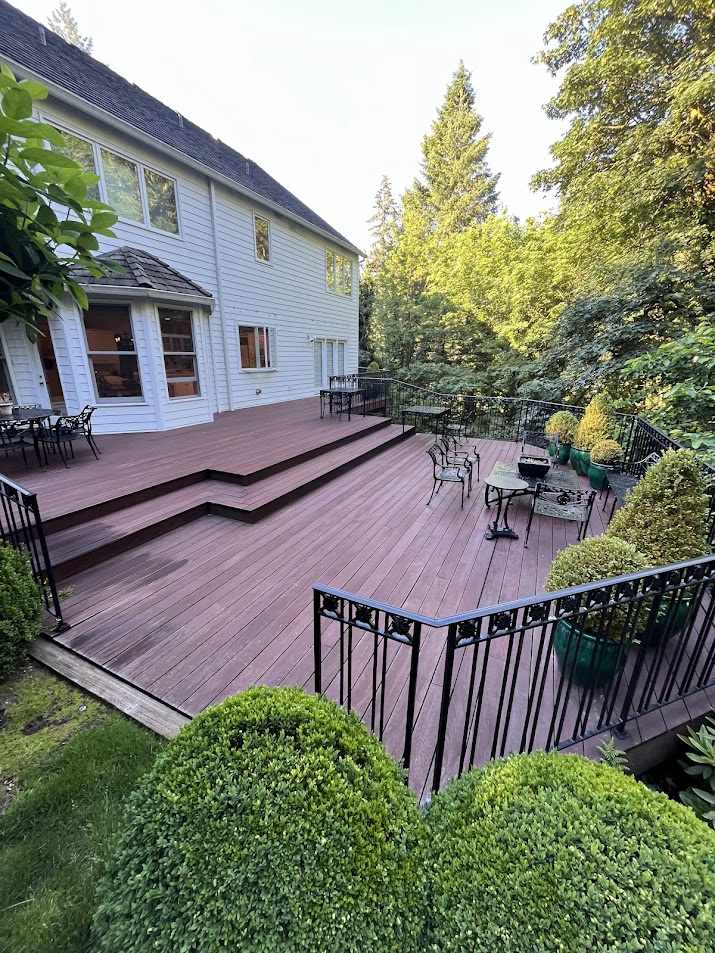 Spacious wooden backyard deck with outdoor furniture, black metal railing, and trimmed bushes at a two-story white house in Herrle—an ideal spot for relaxing or entertaining. Portland painter Pearl Painters can help refresh your deck or exterior.