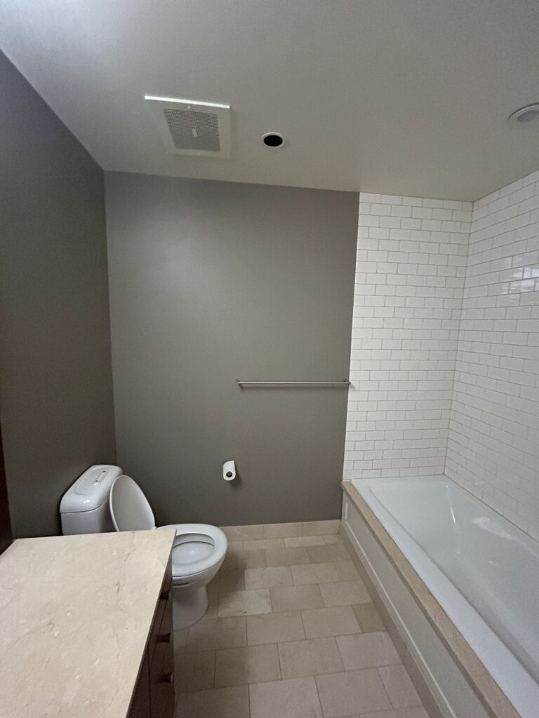 Bathroom with beige tile floor, a toilet, a countertop, and a bathtub with white subway tile surround.