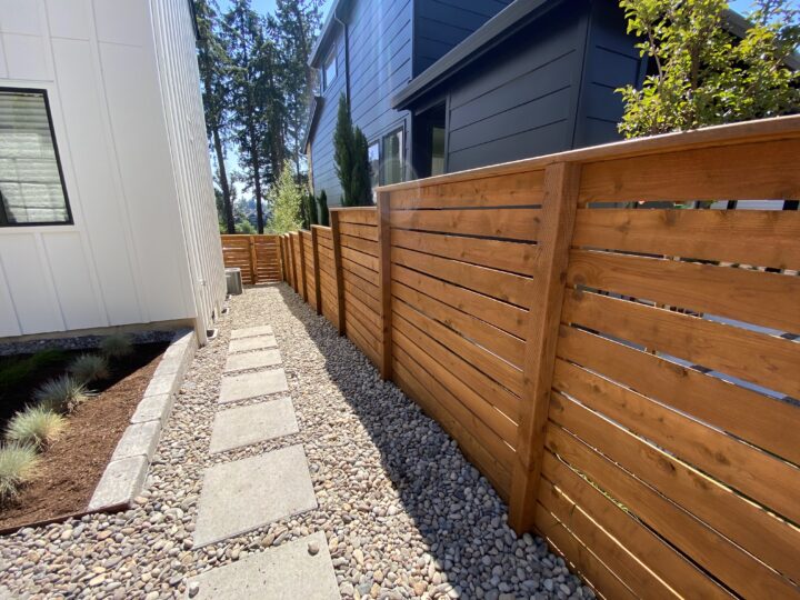 A gravel pathway with concrete stepping stones runs between two modern houses, bordered by a beautifully stained wooden privacy fence on one side.