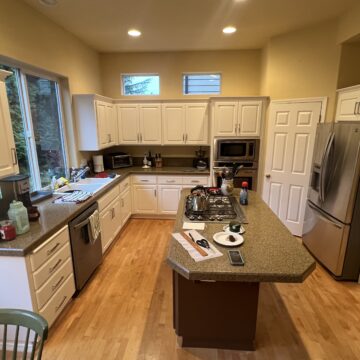 A spacious kitchen with white cabinets, a center island with a cooktop, stainless steel appliances, and wooden floors.