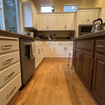 A kitchen with white cabinets, brown island, stainless steel appliances, and wood floors. A tea kettle is on the island, and a towel hangs from the dishwasher.