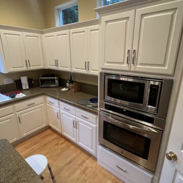 A kitchen with white cabinets, a double wall oven, granite countertops, small appliances, and a door partially visible on the right.