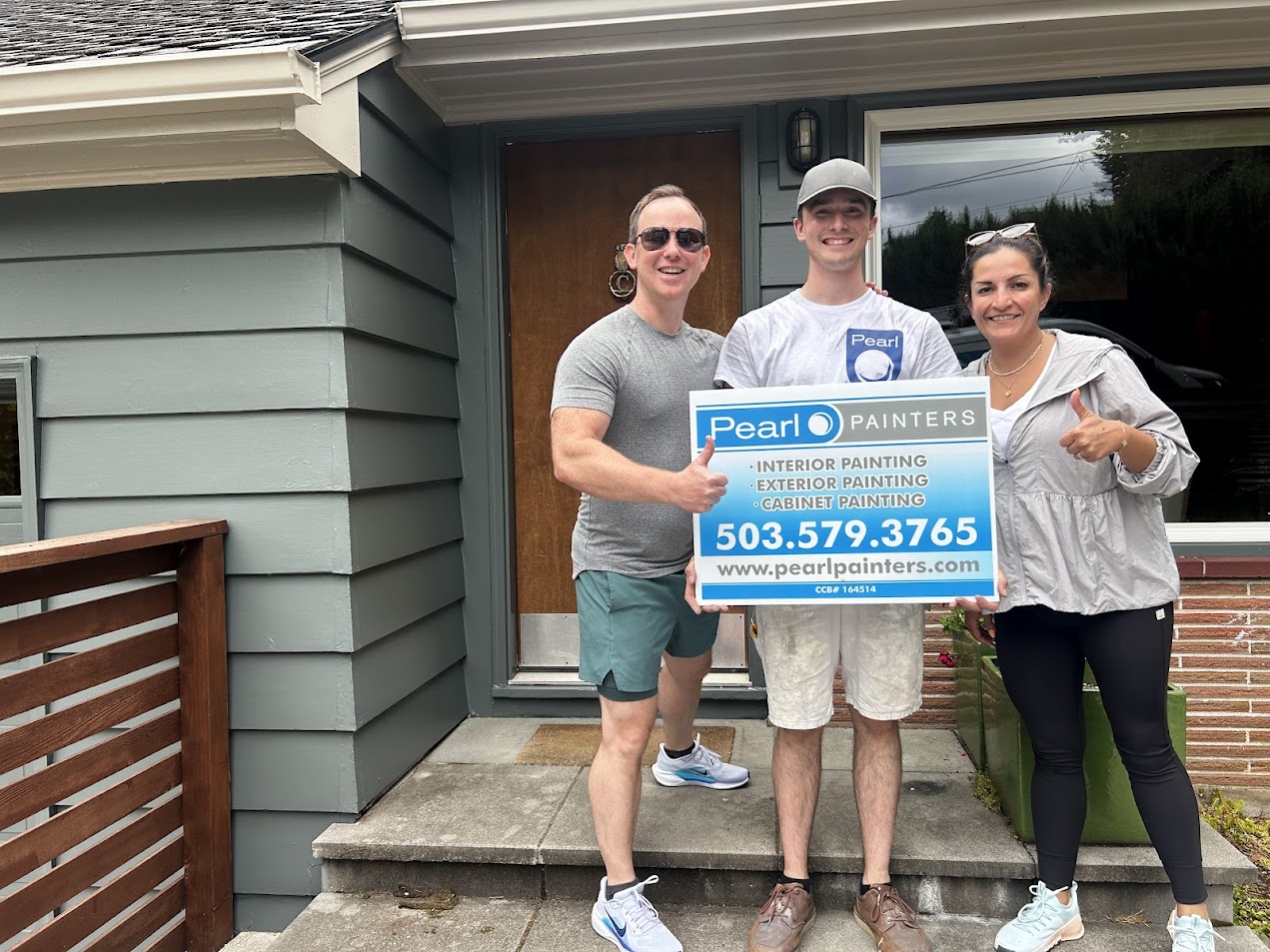 Three people stand outside a Carlton house, holding a Pearl Painters sign for painting services. The sign includes contact details and notes booking into June 2025.