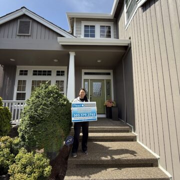 A painter stands on the front steps of a modern Hendricks house in Portland, holding a real estate sign, May 2025. Pearl Painters.