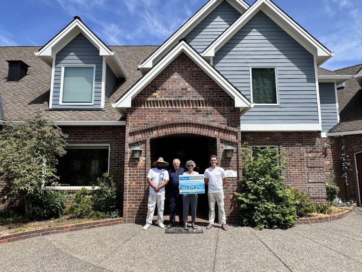 Four people stand in front of a brick house in Portland; two hold a sign with "Anderson ext," phone numbers, and other text. Photo taken June 2025, possibly for Pearl Painters or painting services.