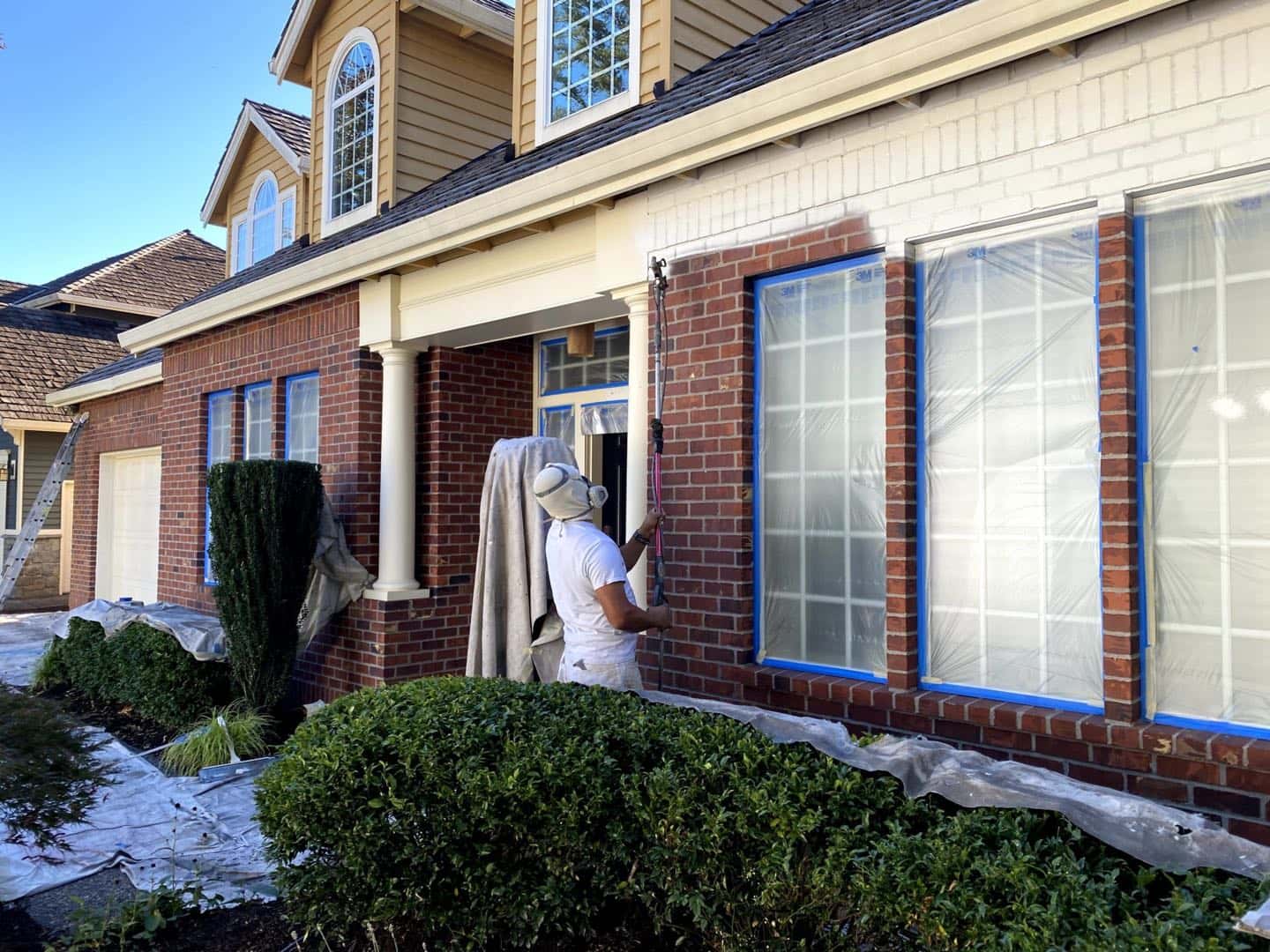 A man painting the exterior of a brick house in Portland