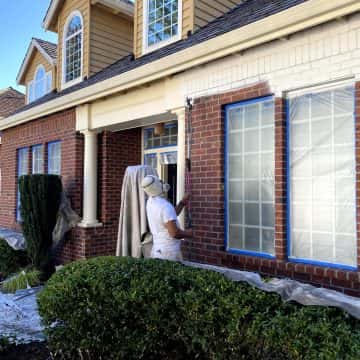 A man painting the exterior of a house with brick siding.