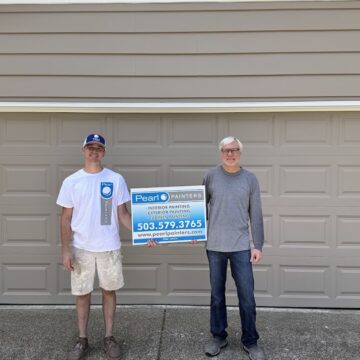 Two painters hold a Pearl Painters sign with contact info in front of a garage door in Cleveland; now booking exterior painting.