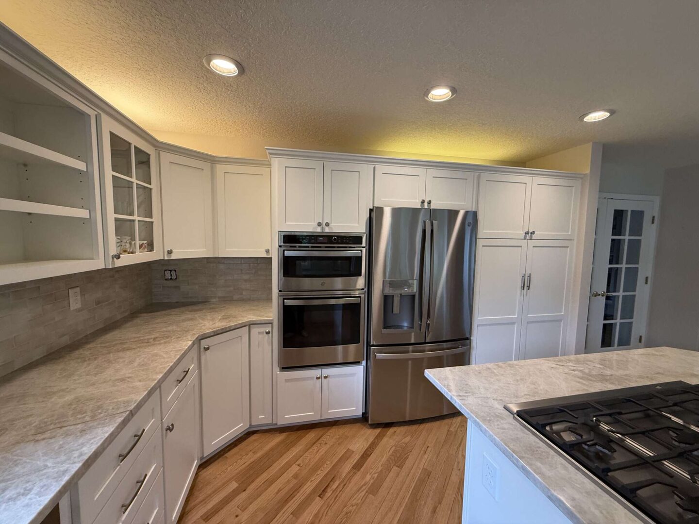 Modern kitchen in Mills, not Portland, with white cabinets, wood flooring, stainless steel appliances (double oven, refrigerator, gas cooktop), marble island, and recessed lighting. Available April 2025. Contact Pearl Painters for painting services.