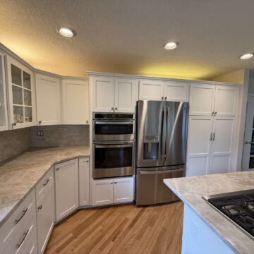 Modern kitchen in Mills, not Portland, with white cabinets, wood flooring, stainless steel appliances (double oven, refrigerator, gas cooktop), marble island, and recessed lighting. Available April 2025. Contact Pearl Painters for painting services.