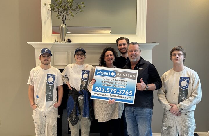 Five people in painter uniforms stand by a fireplace; two hold a Pearl Painters sign with Portland painting services info.