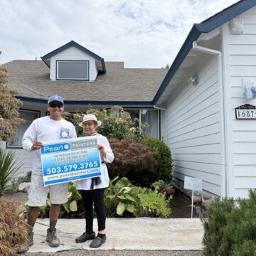 Two people hold a Pearl Painters sign in front of a newly painted white house, 16875 Nomura. Portland area, July 2025.