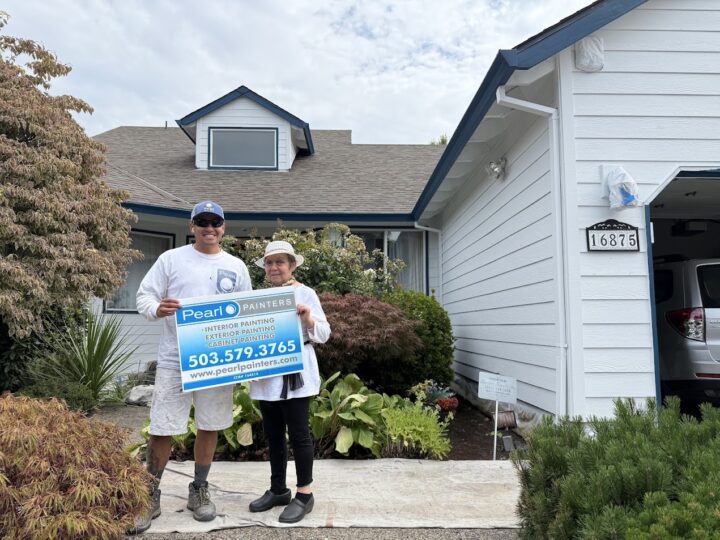 Two people hold a Pearl Painters sign in front of a newly painted white house, 16875 Nomura. Portland area, July 2025.