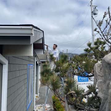 A connected man from Pearl Painters is painting the roof of a house.