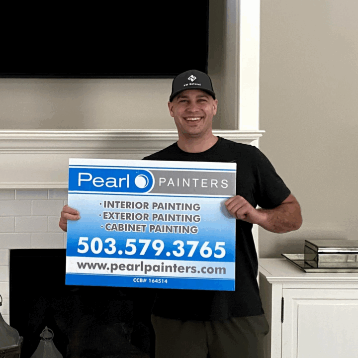 Man holds a Pearl Painters sign for painting services in Portland, showing contact info and website.
