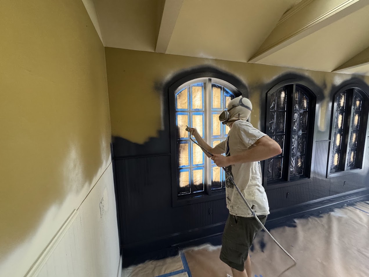 In July 2025, painter Dennis of Pearl Painters in Portland spray-paints an interior wall black, windows and floor taped off.